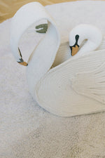 Cesta Swan con un cojín de cisne en su interior, colocada sobre una alfombra clara.