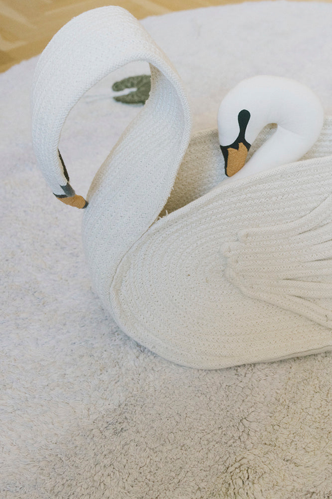 Cesta Swan con un cojín de cisne en su interior, colocada sobre una alfombra clara.