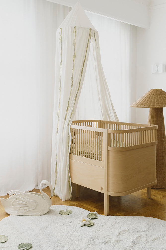 Dosel de crepé marfil sobre una cuna de madera en una habitación infantil.
