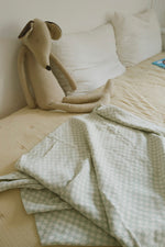 Manta Tiles azul salvia sobre una cama junto a un perro de peluche.