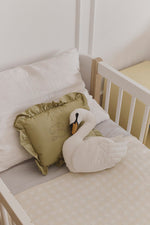 Cojín Swan color marfil junto a un cojín verde con volantes en una cuna blanca.