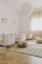 Alfombra Vichy matcha en una habitación infantil luminosa con cuna blanca.
