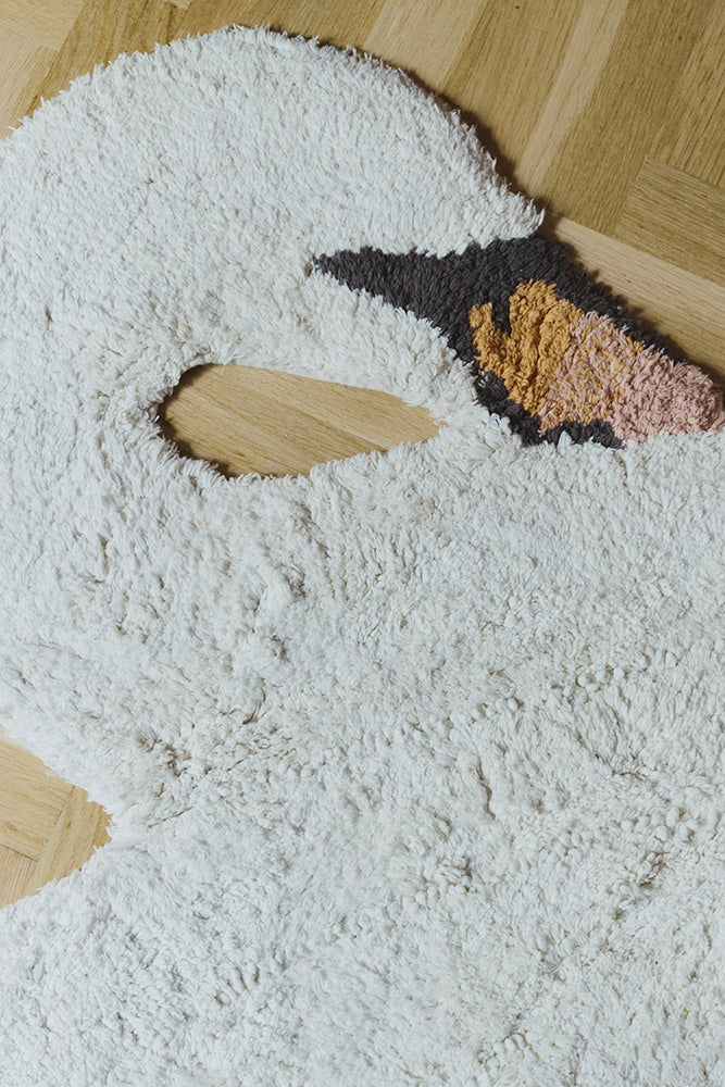 Primer plano de la cabeza y el cuello de la alfombra Swan sobre un suelo de madera, con distintas texturas en tono marfil.