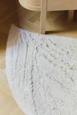 Detalle del ala y la cola de la alfombra Swan, con líneas en relieve y flecos sobre un suelo de madera.
