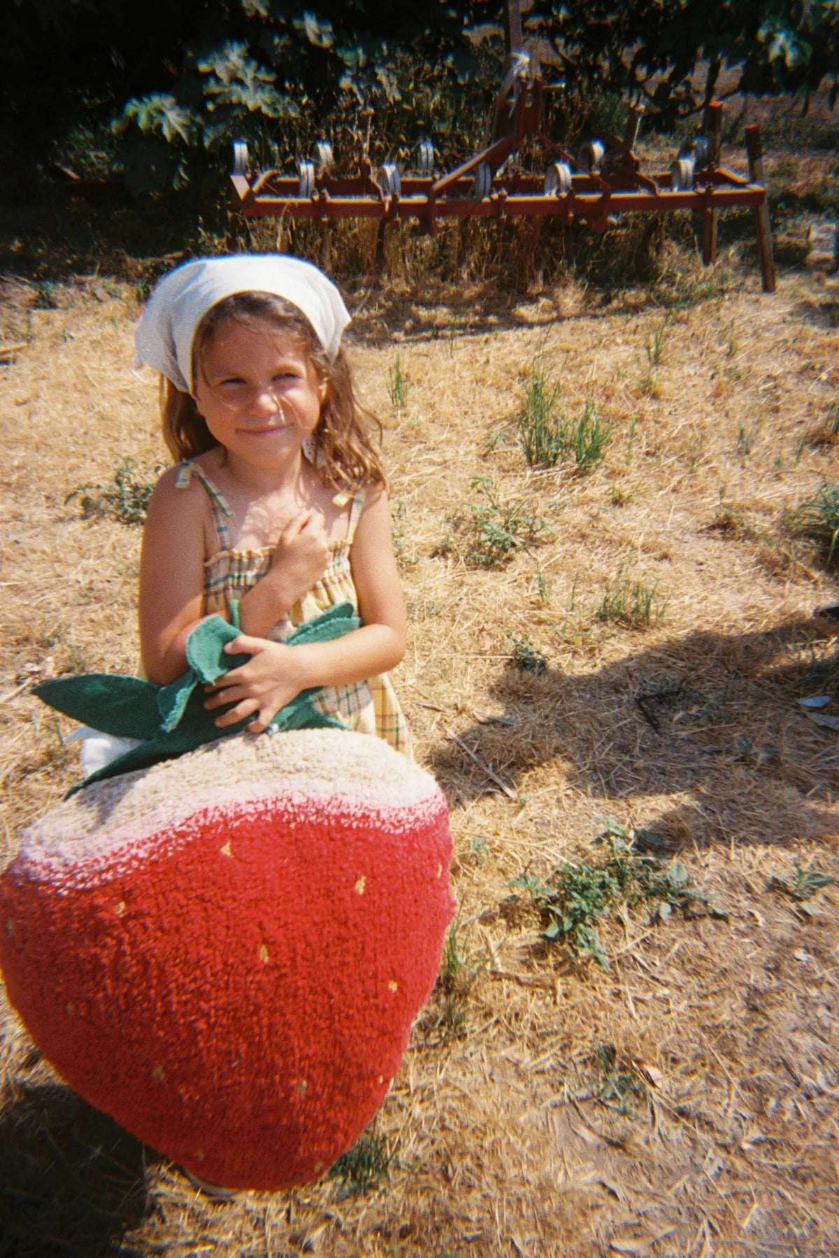 Niña con el cojín Strawberry al aire libre, mostrando su forma de fresa y su parte superior clara.