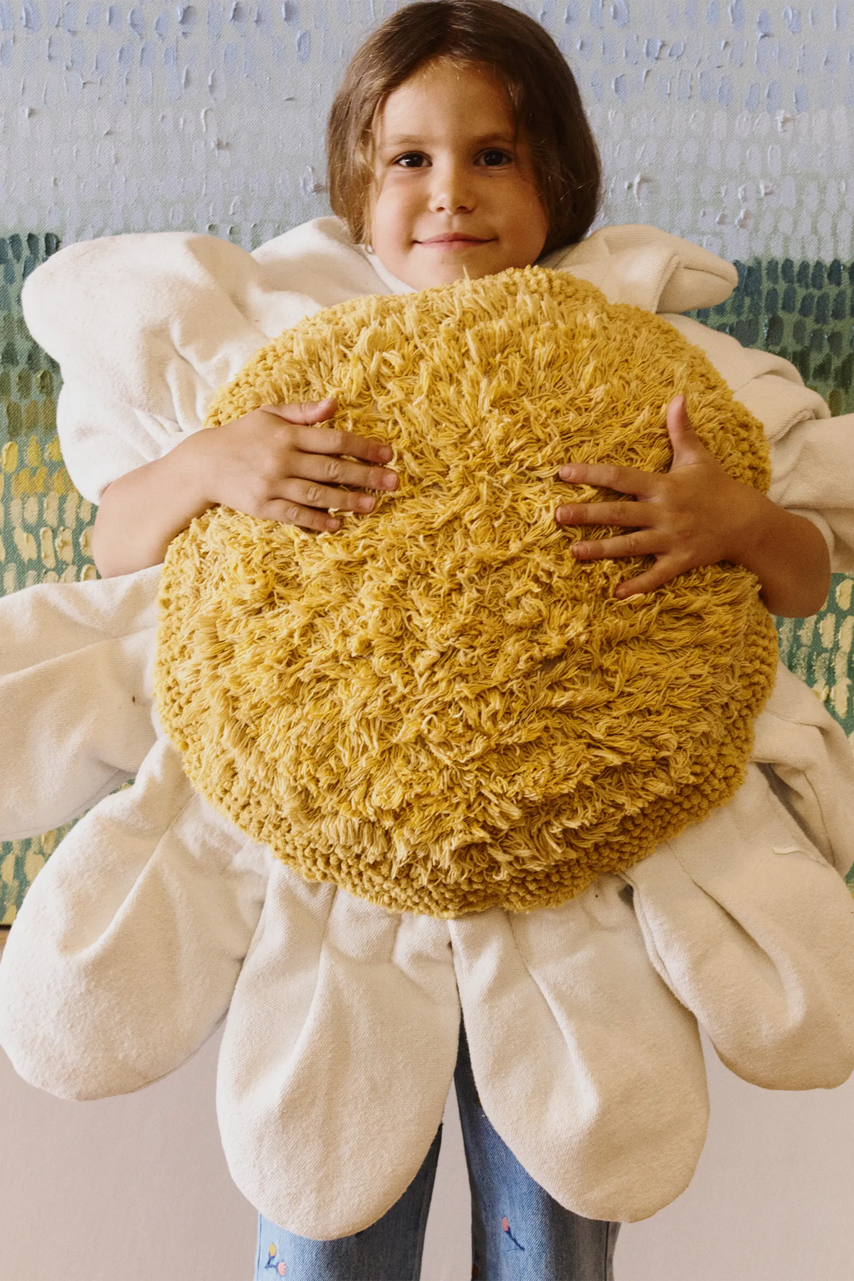 Niña abrazando el cojín de suelo White Daisy, con pétalos claros y centro amarillo con flecos.