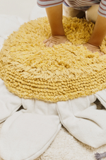 Manos infantiles presionando el centro acolchado amarillo del cojín de suelo White Daisy.