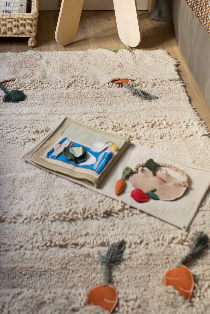 Libro sensorial abierto sobre una alfombra, con verduras de tela, una cesta y una escena de mesa preparada.