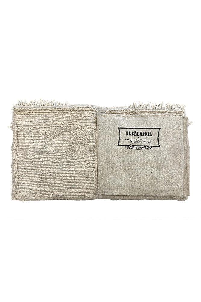 Doble página en tono natural del libro textil, con texturas bordadas y etiqueta de Oli&Carol x Lorena Canals.